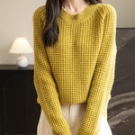 A woman wearing a long sleeve yellow off shoulder merino wool sweater with a ribbed neck.