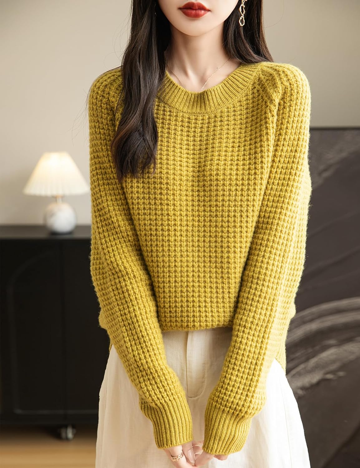 A woman wearing a long sleeve yellow off shoulder merino wool sweater with a ribbed neck.