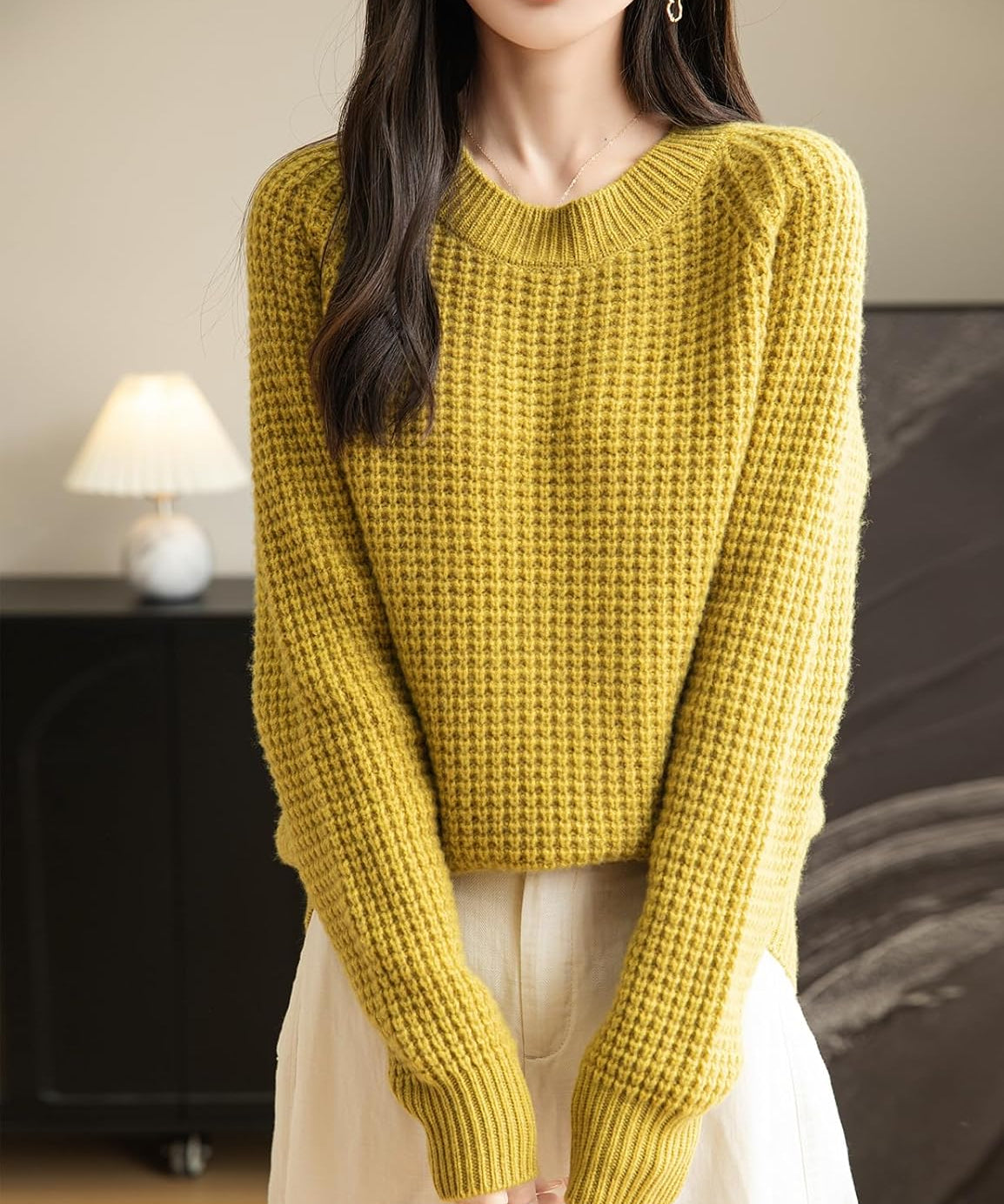 A woman wearing a long sleeve yellow off shoulder merino wool sweater with a ribbed neck.