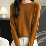 A woman wearing a long sleeve merino wool caramel crewneck sweater.