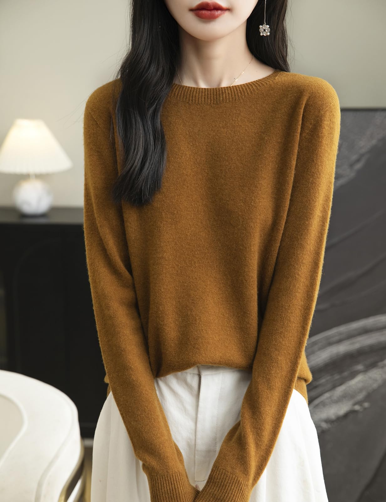 A woman wearing a long sleeve merino wool caramel crewneck sweater.