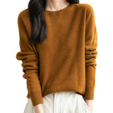 A woman wearing a long sleeve merino wool caramel crewneck sweater.