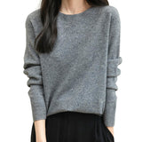A woman wearing a long sleeve merino wool grey crewneck sweater.