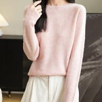 A woman wearing a long sleeve merino wool pink crewneck sweater.