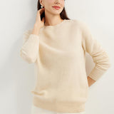A woman wearing a beige, long-sleeved, crew neck cashmere sweater.
