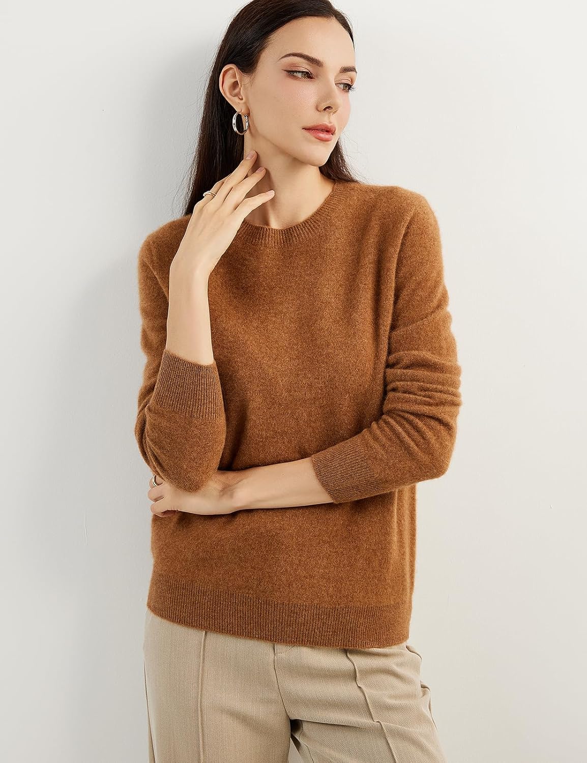 A woman wearing a caramel, long-sleeved, crew neck cashmere sweater.