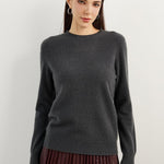 A woman wearing a dark grey, long-sleeved, crew neck cashmere sweater.