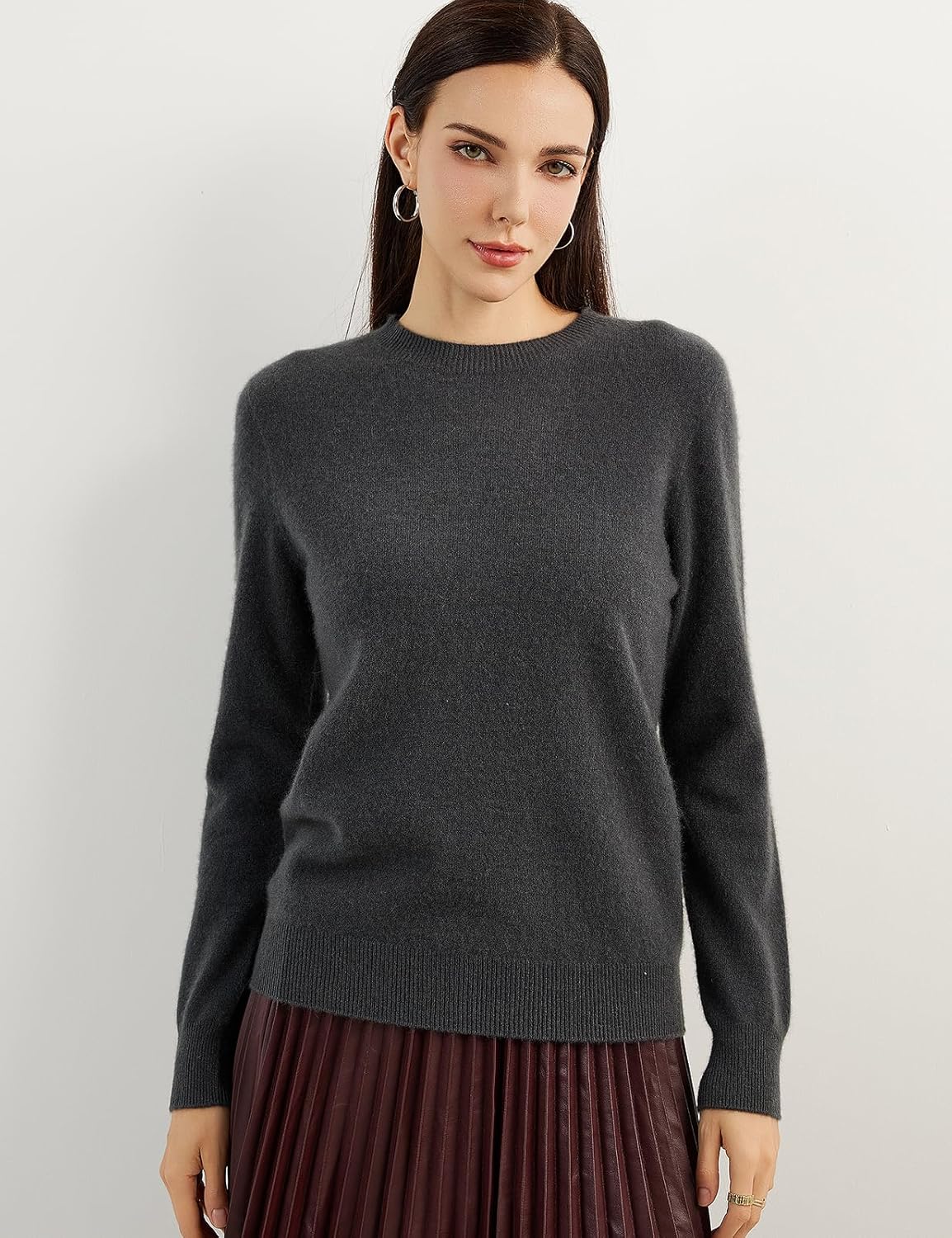 A woman wearing a dark grey, long-sleeved, crew neck cashmere sweater.