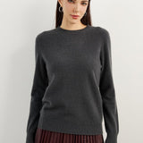 A woman wearing a dark grey, long-sleeved, crew neck cashmere sweater.