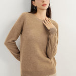 A woman wearing a tan,  long-sleeved, crew neck cashmere sweater.